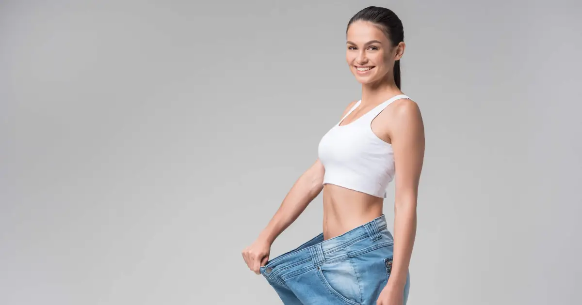 Woman showing weight loss by holding out loose jeans, demonstrating progress after Medical Weight Loss program in Loveland, CO